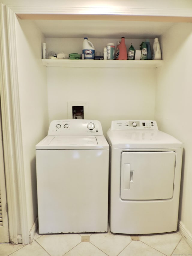 clothes washing area featuring light tile patterned flooring, laundry area, washing machine and clothes dryer, and baseboards