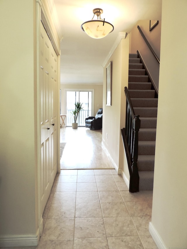 hallway featuring stairs, baseboards, and light tile patterned flooring