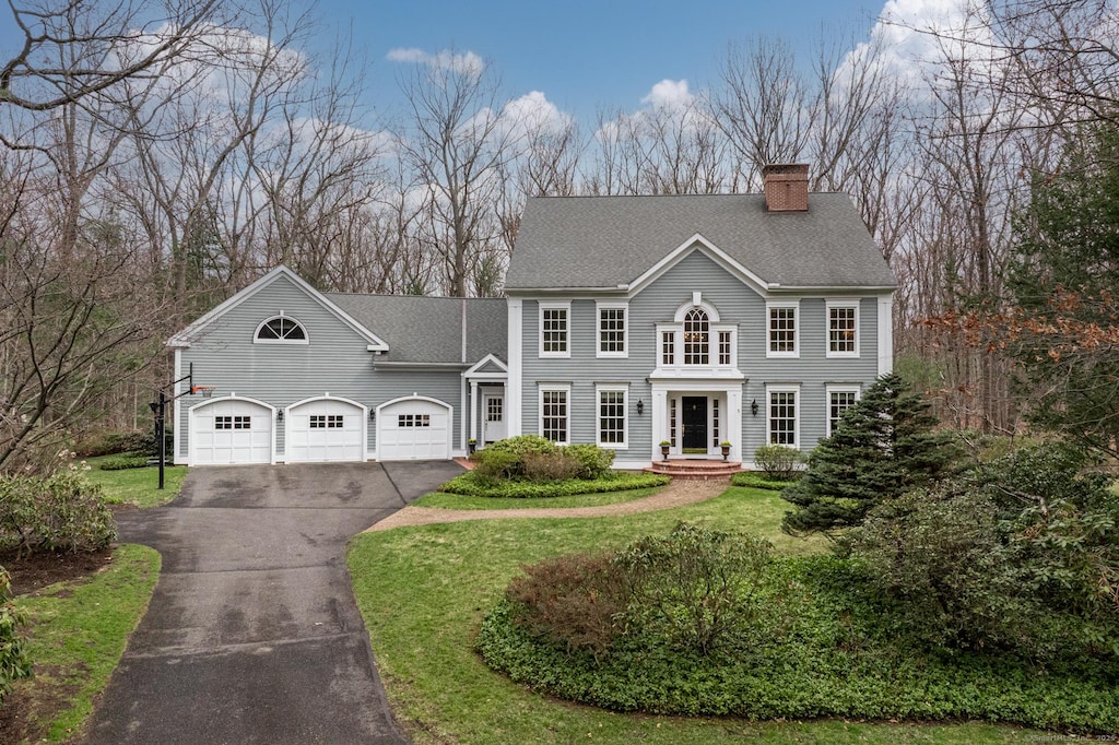 view of front of property with a front yard, an attached garage, a chimney, aphalt driveway, and roof with shingles