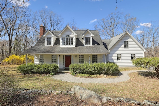 new england style home featuring a porch, roof with shingles, and a chimney