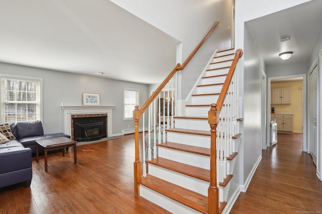 stairway featuring a brick fireplace, baseboard heating, wood finished floors, and baseboards