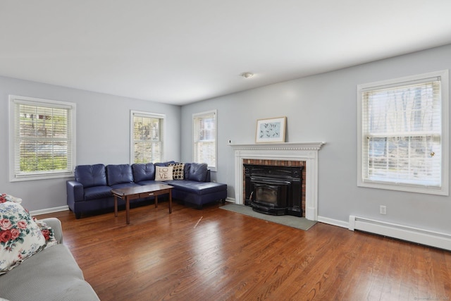 living room featuring a baseboard radiator, a healthy amount of sunlight, wood finished floors, and a brick fireplace