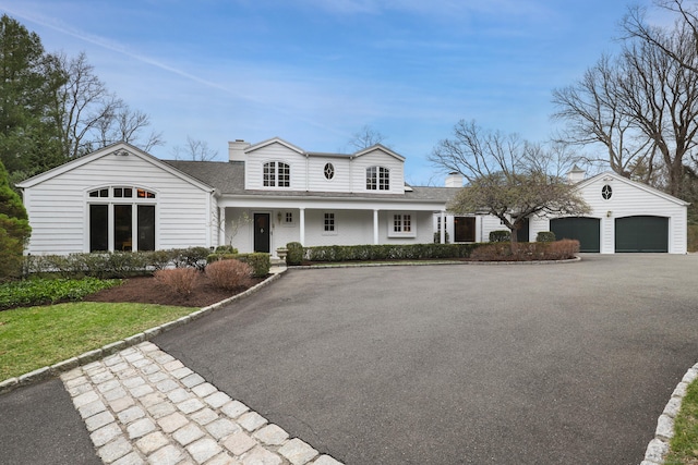 view of front of property featuring a porch, roof with shingles, an attached garage, a chimney, and driveway