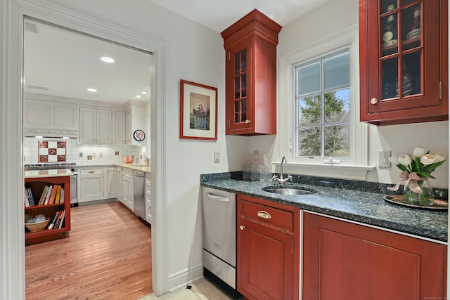 kitchen with glass insert cabinets, a sink, dark stone counters, stainless steel appliances, and decorative backsplash