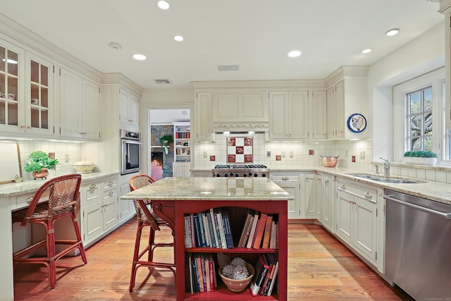 kitchen with open shelves, a sink, appliances with stainless steel finishes, light wood-style flooring, and light stone counters