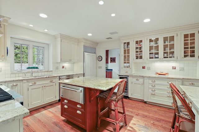 kitchen with a sink, wine cooler, a warming drawer, light wood finished floors, and light stone countertops