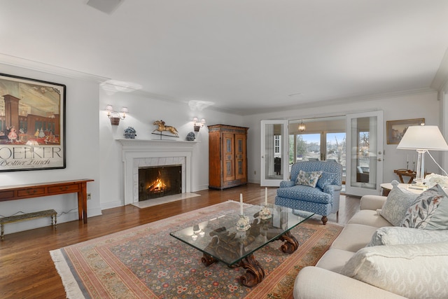living area featuring a tiled fireplace, ornamental molding, baseboards, and wood finished floors