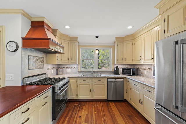 kitchen with tasteful backsplash, a sink, appliances with stainless steel finishes, premium range hood, and cream cabinets