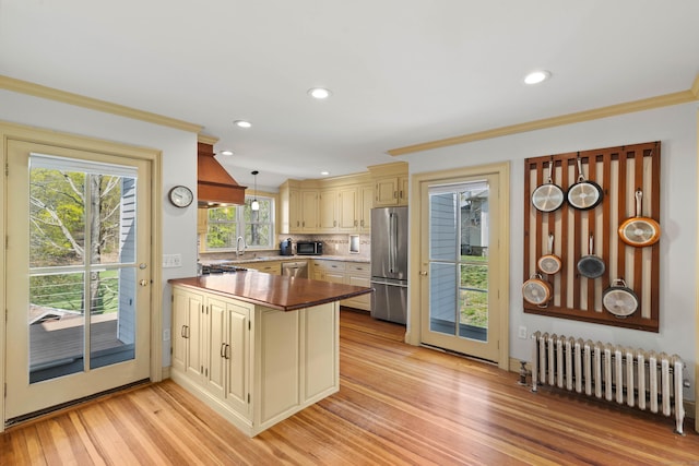 kitchen with cream cabinets, light wood-style flooring, appliances with stainless steel finishes, radiator, and a peninsula