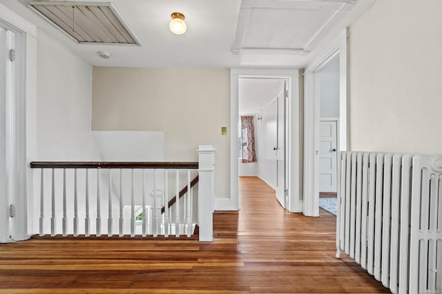 hallway with an upstairs landing, radiator heating unit, wood finished floors, and attic access
