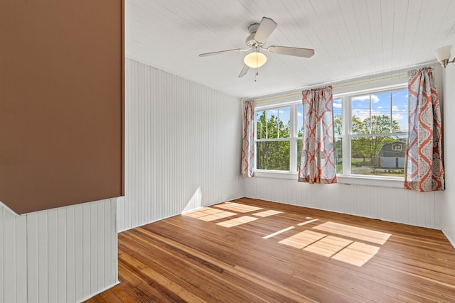 unfurnished room featuring wood walls, wood finished floors, and ceiling fan