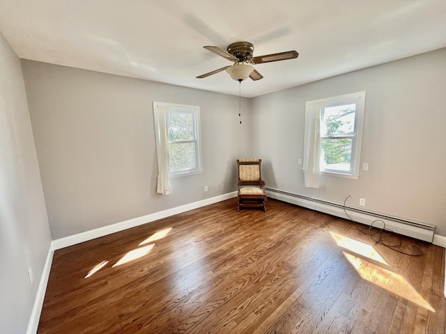 unfurnished room featuring a healthy amount of sunlight, a baseboard radiator, baseboards, and wood finished floors