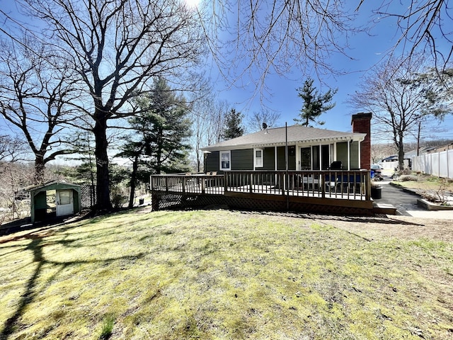 back of house featuring an outbuilding, a deck, a chimney, and a lawn