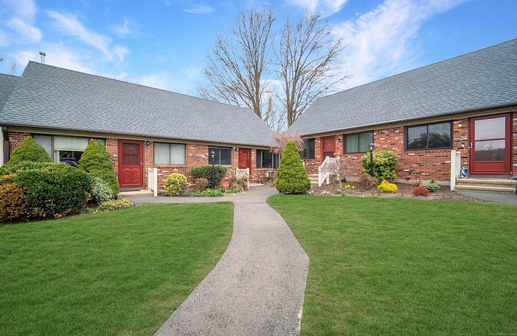 view of front of home featuring a shingled roof, a front lawn, and brick siding