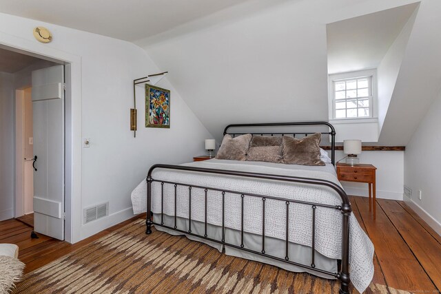 bedroom featuring baseboards, lofted ceiling, wood finished floors, and visible vents