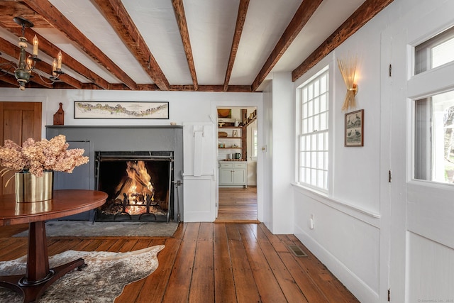 living room featuring plenty of natural light, a fireplace with flush hearth, beamed ceiling, visible vents, and hardwood / wood-style flooring