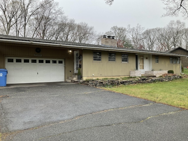 single story home with an attached garage, driveway, a chimney, and a front lawn