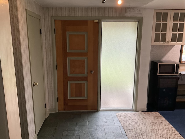 doorway to outside with wallpapered walls and stone tile floors