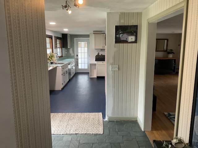 kitchen featuring wallpapered walls, light countertops, stainless steel dishwasher, a sink, and baseboards