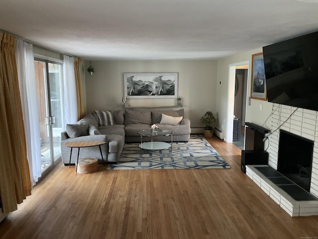 living room featuring a baseboard heating unit, wood finished floors, and a fireplace with raised hearth