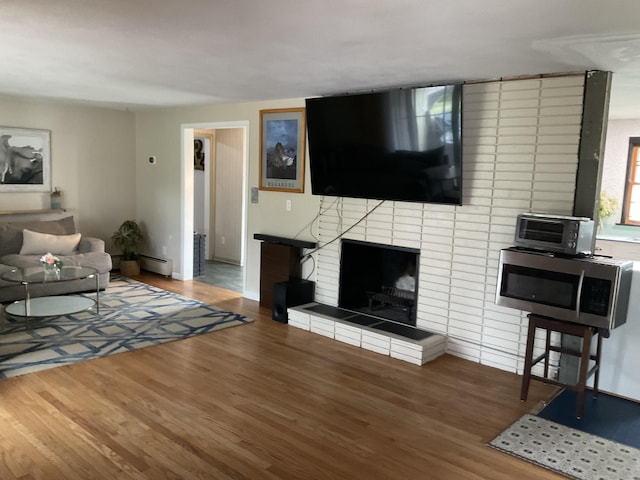 living room with baseboard heating, wood finished floors, a toaster, a fireplace, and baseboards