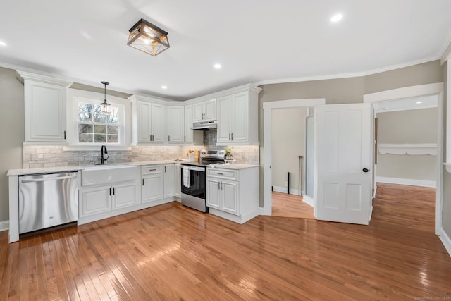 kitchen with tasteful backsplash, under cabinet range hood, appliances with stainless steel finishes, light wood finished floors, and crown molding