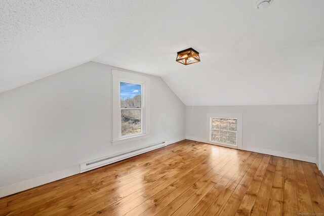 bonus room featuring baseboard heating, baseboards, light wood finished floors, and vaulted ceiling