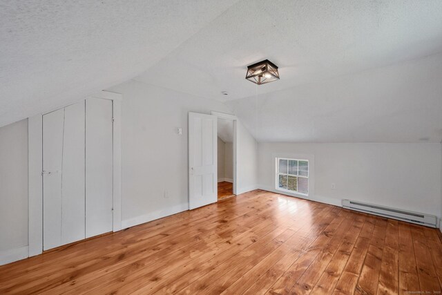 additional living space with a baseboard heating unit, light wood-style floors, a textured ceiling, and lofted ceiling
