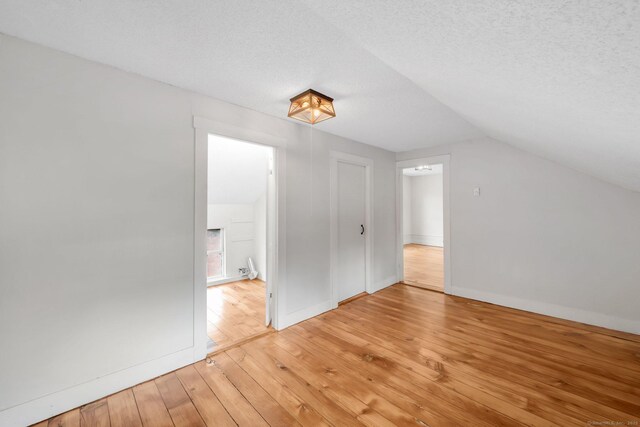 additional living space with a textured ceiling, lofted ceiling, and light wood-style flooring