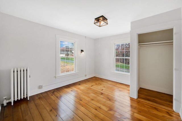 unfurnished bedroom with radiator, a closet, hardwood / wood-style flooring, and baseboards