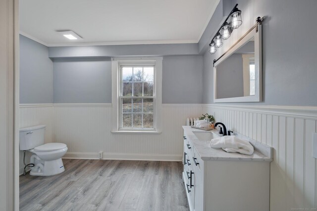 bathroom with vanity, toilet, crown molding, wainscoting, and wood finished floors