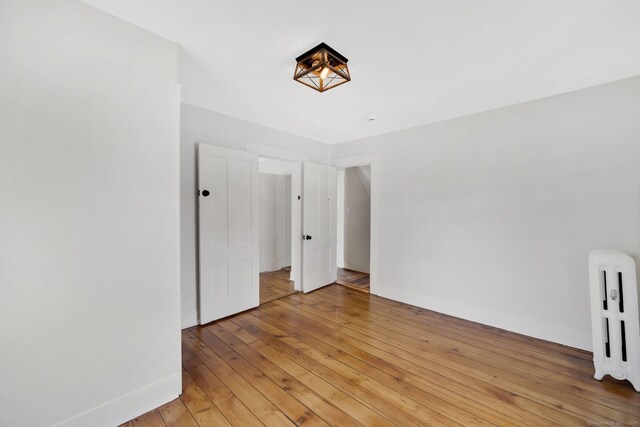 unfurnished bedroom with light wood-type flooring, baseboards, and radiator