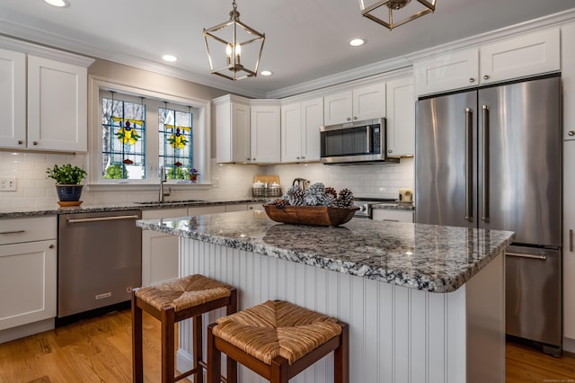 kitchen with appliances with stainless steel finishes, a sink, white cabinetry, decorative backsplash, and ornamental molding