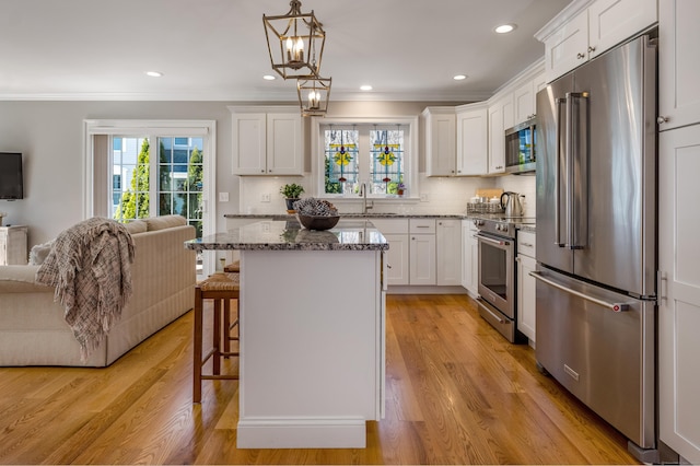 kitchen with a breakfast bar area, stone countertops, open floor plan, premium appliances, and ornamental molding