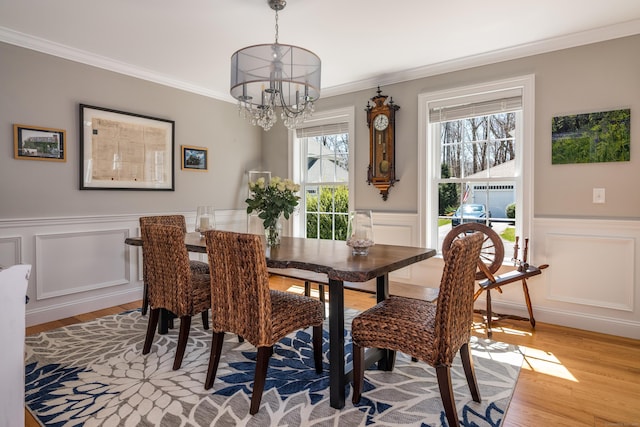 dining space featuring crown molding, an inviting chandelier, wainscoting, a decorative wall, and light wood-type flooring