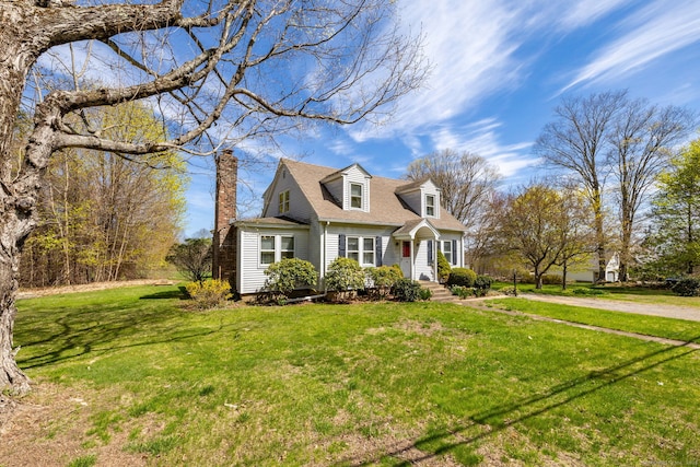 new england style home featuring roof with shingles, a chimney, and a front lawn