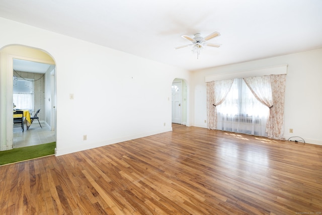empty room with arched walkways, ceiling fan, wood finished floors, and a healthy amount of sunlight