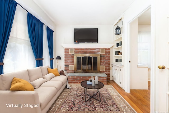 living area featuring a healthy amount of sunlight, a brick fireplace, and wood finished floors