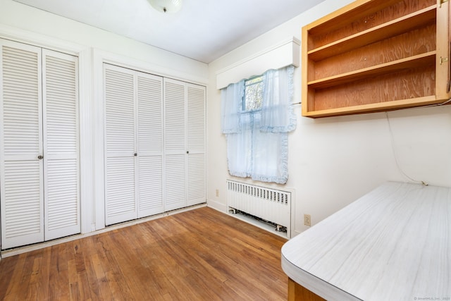 unfurnished bedroom with multiple closets, wood finished floors, and radiator