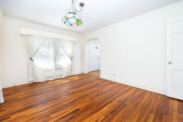 spare room featuring arched walkways, baseboards, and wood finished floors