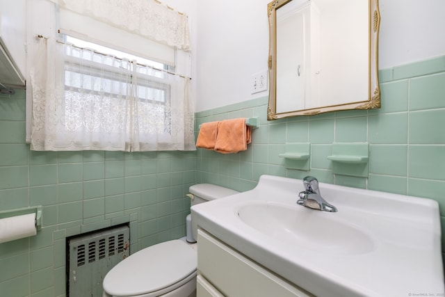 half bath with radiator heating unit, tile walls, vanity, and toilet