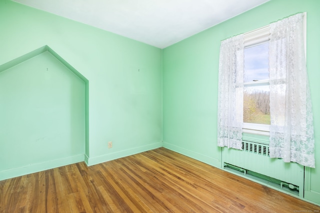 spare room with radiator, baseboards, and wood finished floors