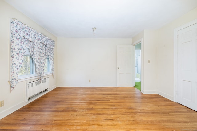 unfurnished room featuring radiator heating unit, baseboards, and light wood-style floors
