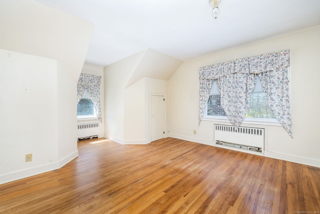 additional living space featuring light wood-style floors, baseboards, and radiator heating unit