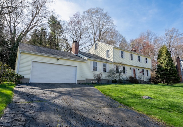 colonial-style house featuring a front yard, an attached garage, a chimney, and driveway