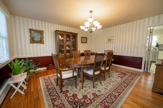 dining area with baseboard heating, wood finished floors, wallpapered walls, a wainscoted wall, and a notable chandelier