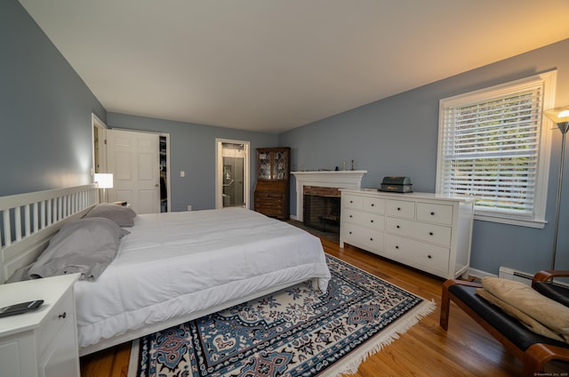 bedroom featuring a baseboard radiator, baseboards, wood finished floors, and a fireplace