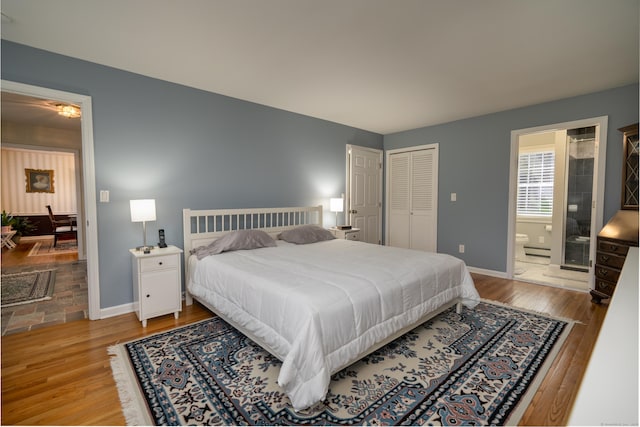 bedroom featuring baseboards, baseboard heating, wood finished floors, and ensuite bathroom
