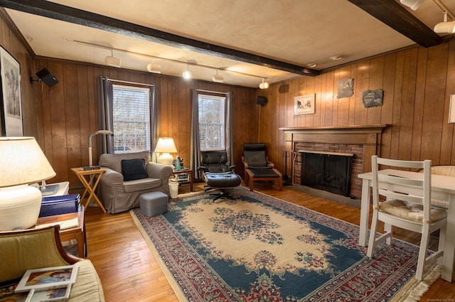 living area with hardwood / wood-style floors, wooden walls, track lighting, a fireplace, and beam ceiling