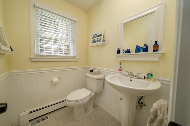 half bathroom featuring tile patterned floors, a wainscoted wall, visible vents, toilet, and a baseboard heating unit